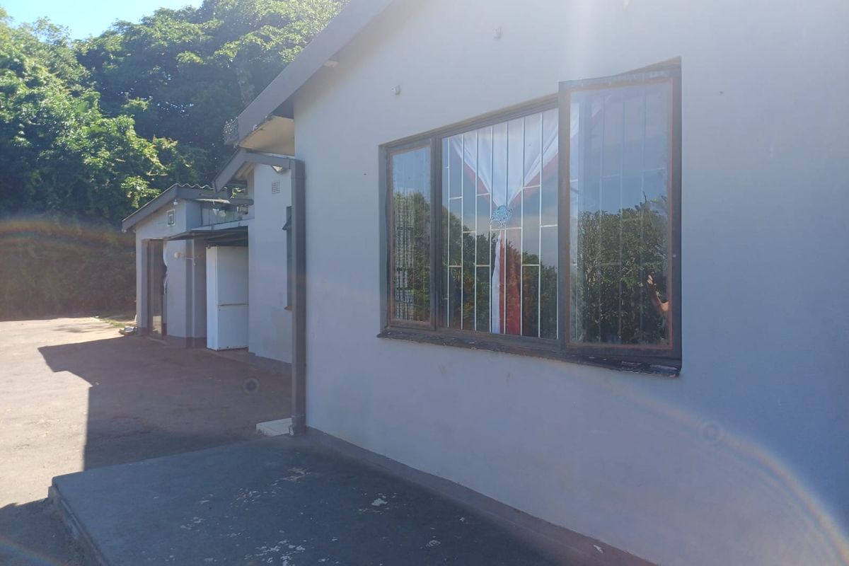A view of the rear exterior of the house featuring a concrete apron, security bars on the windows, and a downpipe.