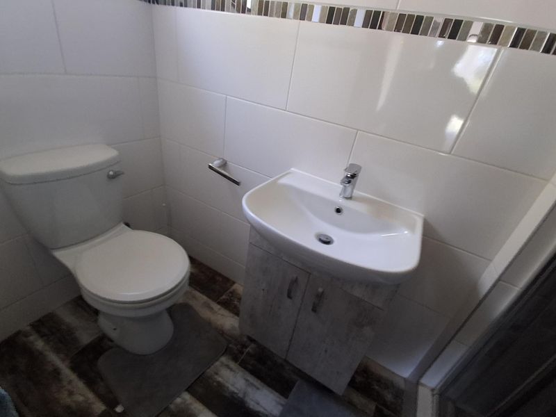 A compact bathroom featuring a modern vanity basin, toilet, and neutral wall tiling with a decorative mosaic border.