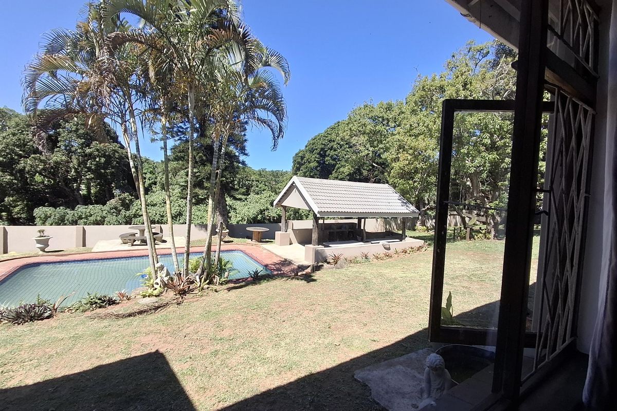 A spacious rear garden featuring a swimming pool with a safety net and a covered lapa area, set against a backdrop of mature trees.