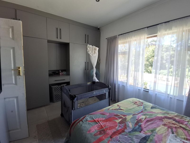 A well-lit bedroom featuring extensive built-in cupboards, tiled flooring, and a large window with security bars, offering a functional and comfortable living space.