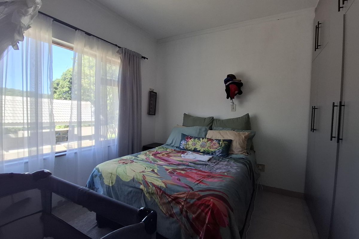 A well-lit bedroom featuring built-in cupboards, tiled flooring, and a large window providing natural light.