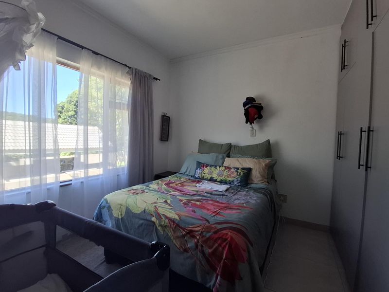 A well-lit bedroom featuring built-in cupboards, tiled flooring, and a large window providing natural light.