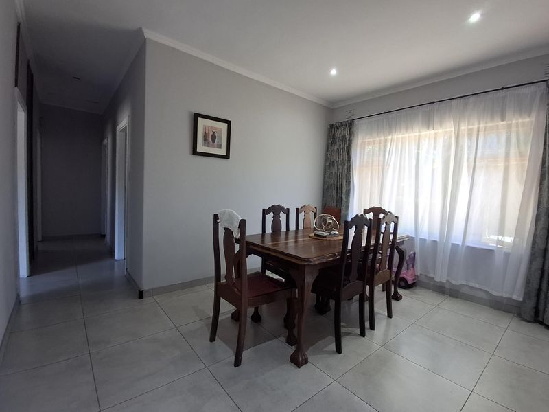 A well-lit dining room featuring neutral tiled flooring and large windows with curtain rails, providing a clean and functional space for family meals.