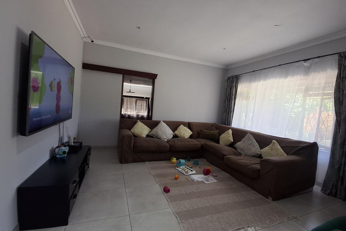 A spacious living room featuring neutral tiled flooring, recessed lighting, and a sliding door, providing a comfortable and functional family living area.