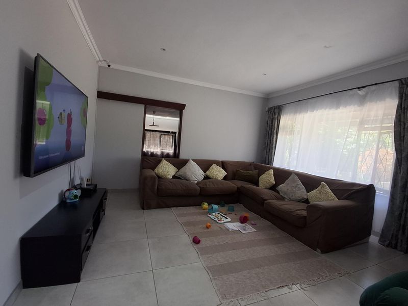 A spacious living room featuring neutral tiled flooring, recessed lighting, and a sliding door, providing a comfortable and functional family living area.