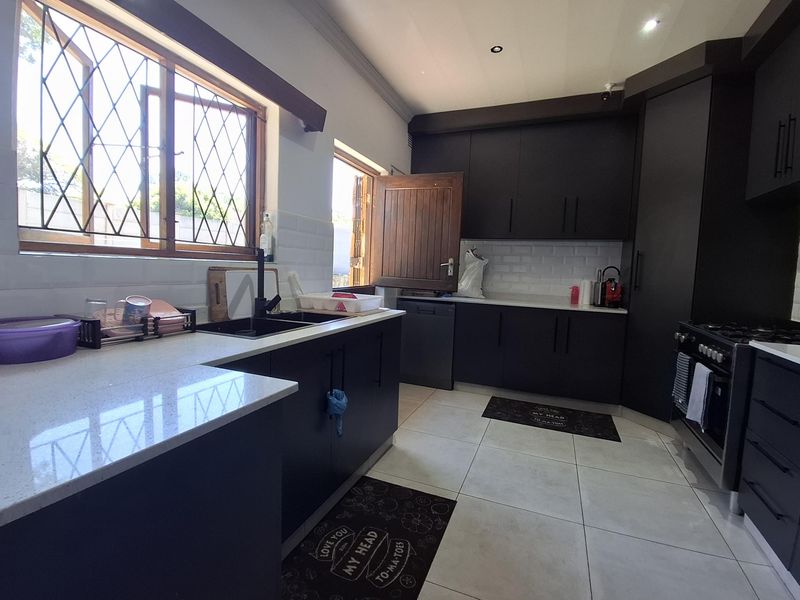 Modern kitchen featuring dark cabinetry, stone countertops, subway tile backsplash, and a gas stove, with ample natural light from the windows.