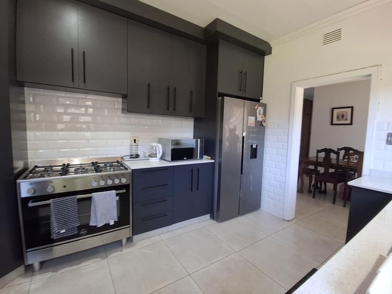 Modern kitchen featuring dark cabinetry, stone countertops, subway tile backsplash, and a stainless steel gas stove, with an open flow to the dining area.