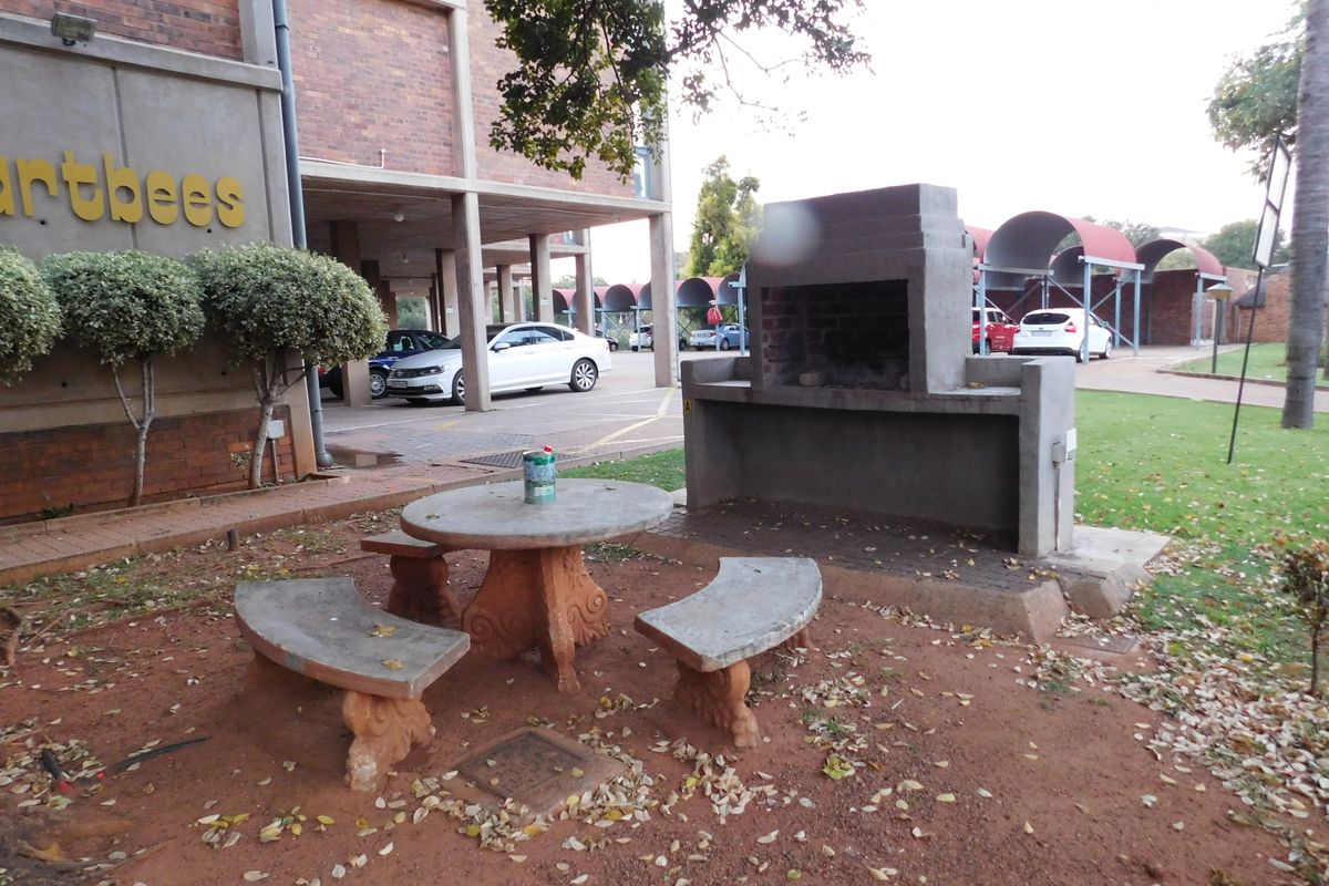Outdoor communal area featuring a built-in brick braai, concrete table, and bench seating set against a brick apartment building facade.