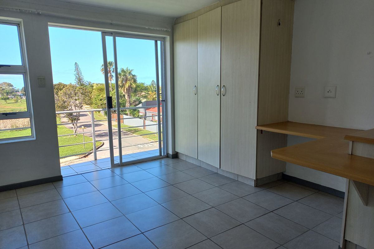 A bright, empty bedroom featuring tiled flooring, built-in cupboards, a built-in desk, and a sliding door leading to a balcony with outdoor views.