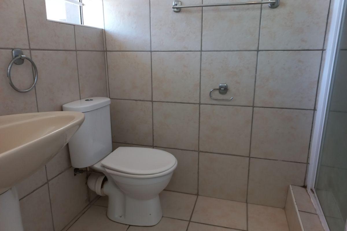 A functional bathroom featuring a pedestal basin, toilet, and shower enclosure with neutral wall and floor tiling.