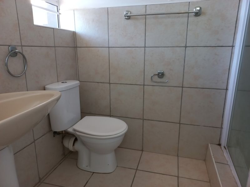 A functional bathroom featuring a pedestal basin, toilet, and shower enclosure with neutral wall and floor tiling.
