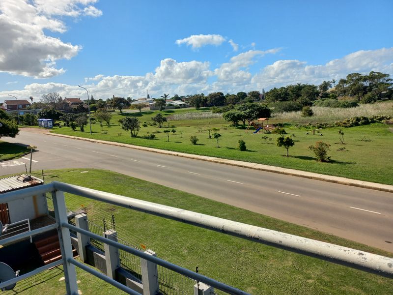 Elevated view from a balcony overlooking a suburban street, green parkland, and playground area.