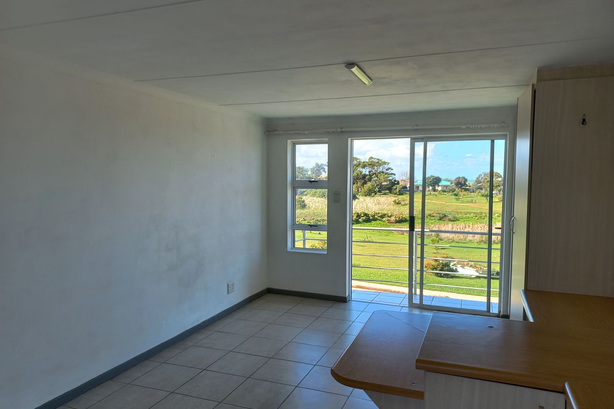 An empty open-plan living area featuring tiled floors, built-in cabinetry, and a sliding glass door leading to a balcony with scenic views.