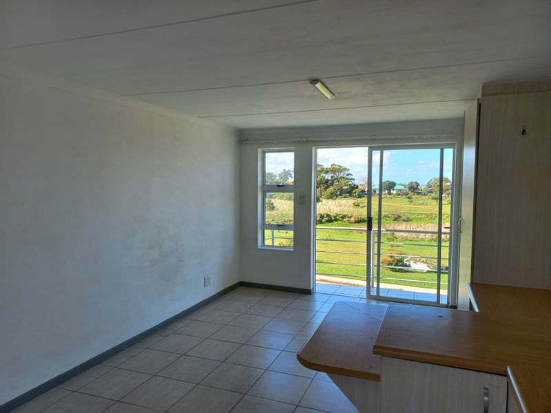 An empty open-plan living area featuring tiled floors, built-in cabinetry, and a sliding glass door leading to a balcony with scenic views.