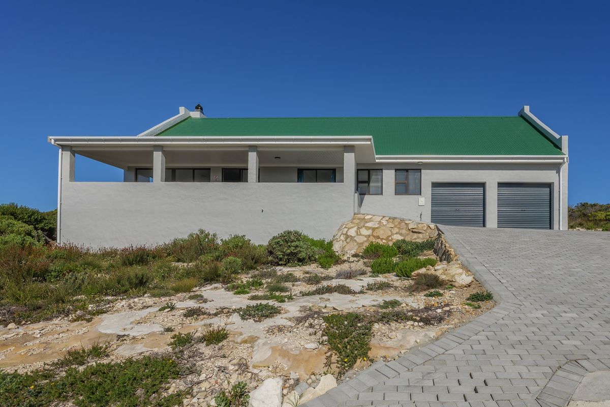 Front elevation of a modern house featuring a green corrugated metal roof, double garage, paved driveway, and a covered patio area.