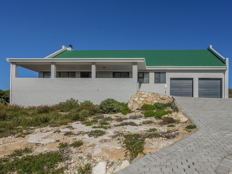 Front elevation of a modern house featuring a green corrugated metal roof, double garage, paved driveway, and a covered patio area.