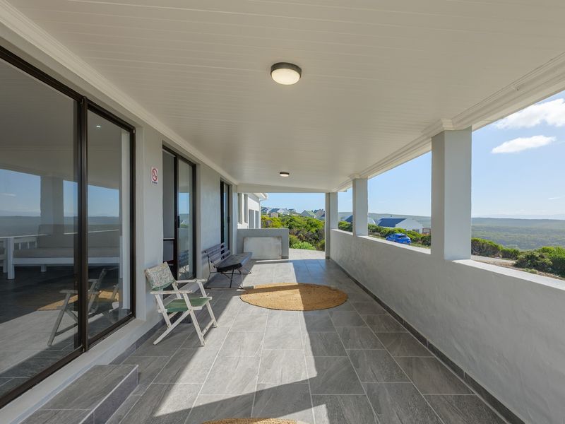 A spacious covered patio featuring modern tiled flooring, sliding glass doors, and a masonry balustrade, offering expansive views of the surrounding landscape.