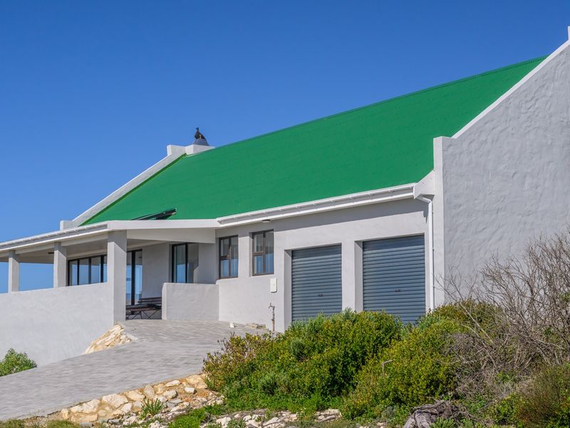 A well-maintained house featuring a distinctive green metal roof, double garage, and a covered patio area with a paved driveway.