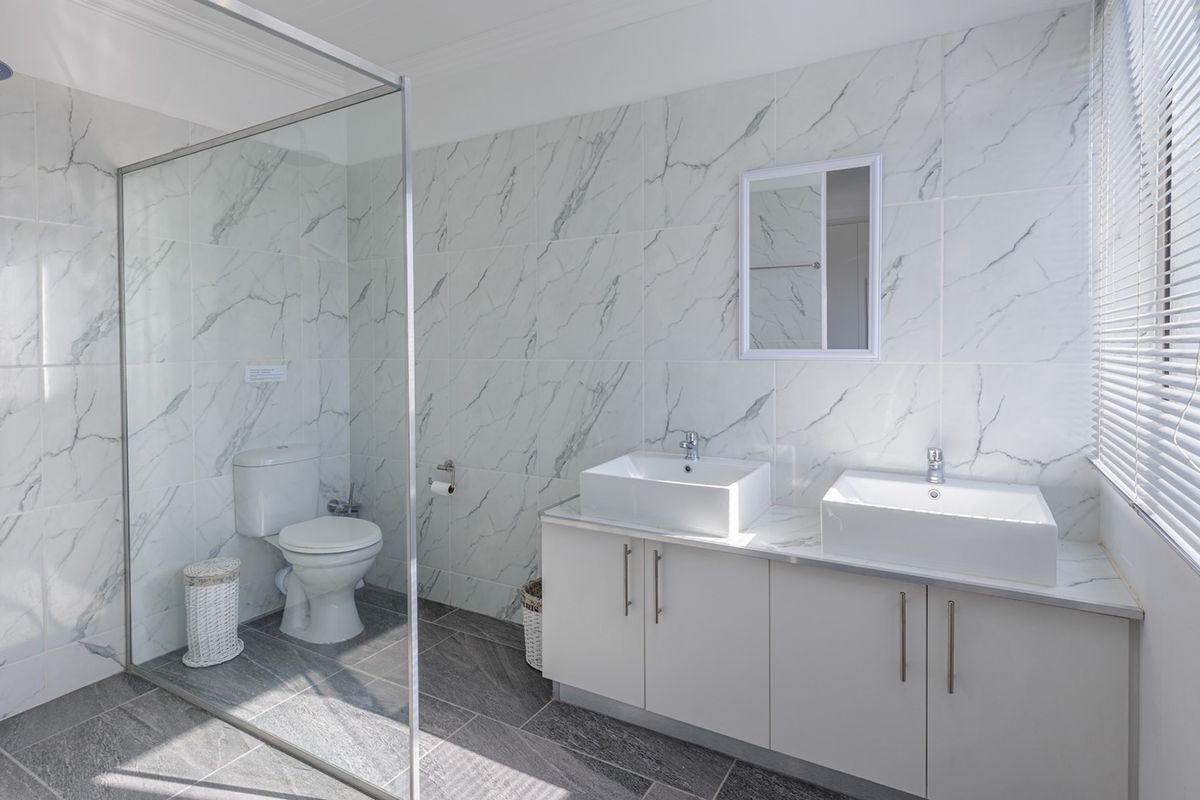 Modern bathroom featuring a double vanity with vessel sinks, a spacious walk-in shower with glass screen, and contemporary marble-look wall tiling.