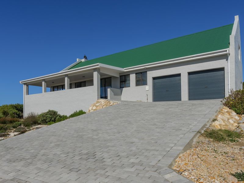 Front view of a modern house featuring a double garage, paved driveway, and a covered patio area with a green metal roof.