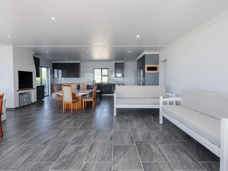 Spacious open-plan living and dining area featuring modern grey floor tiles, a tongue and groove ceiling, and a sleek integrated kitchen.