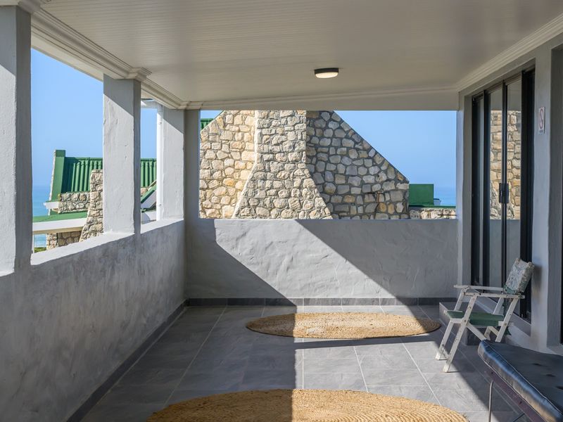 A spacious covered balcony featuring tiled flooring, masonry columns, and sliding glass doors, offering an open-air space with views of the surrounding area.