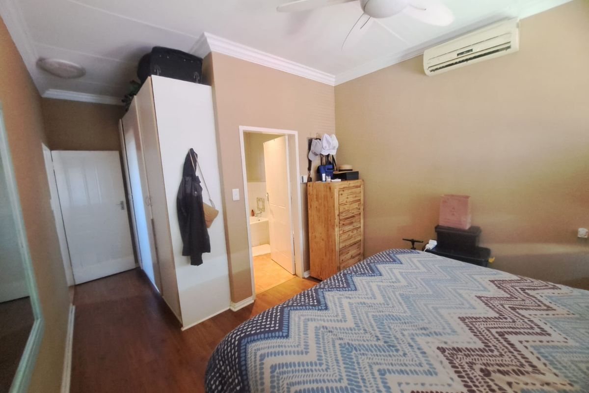 A functional bedroom featuring laminate flooring, a built-in wardrobe, ceiling fan, and a wall-mounted air conditioning unit, with an adjoining en-suite bathroom.