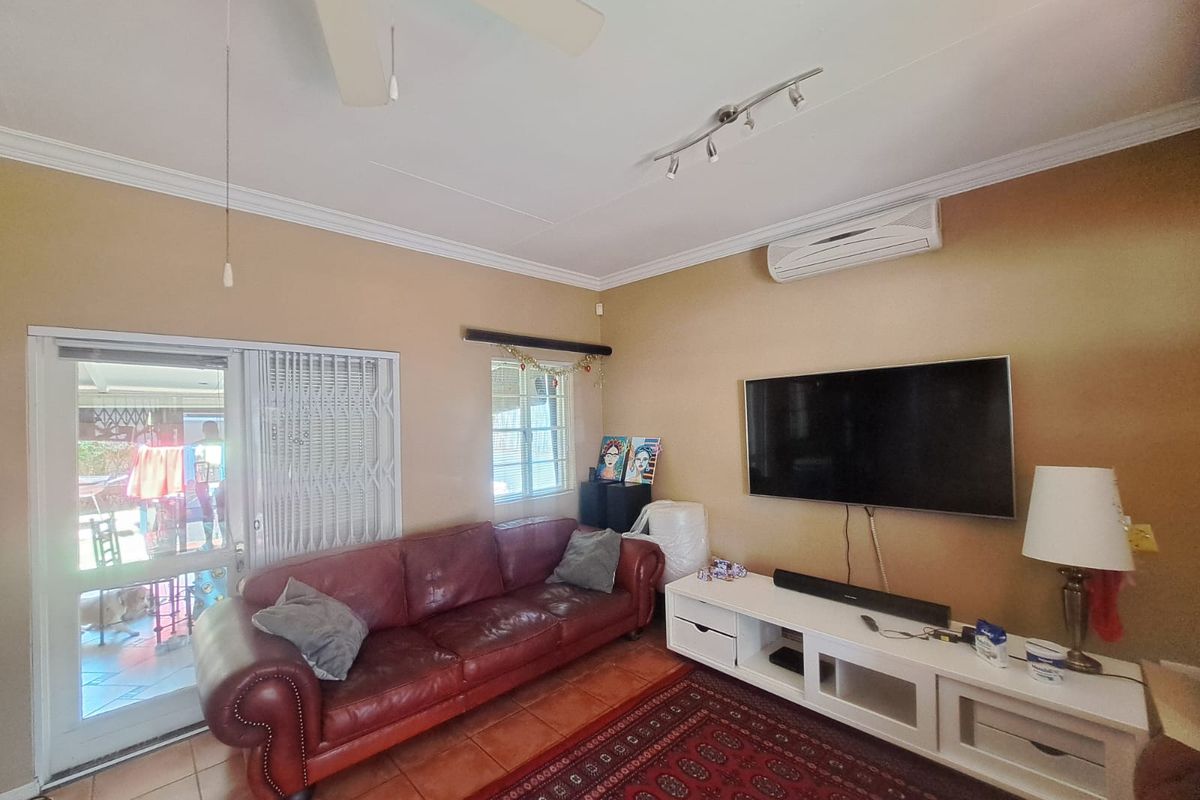 A comfortable living room featuring tiled floors, a ceiling fan, and a wall-mounted air conditioning unit, with direct access to an outdoor patio area.