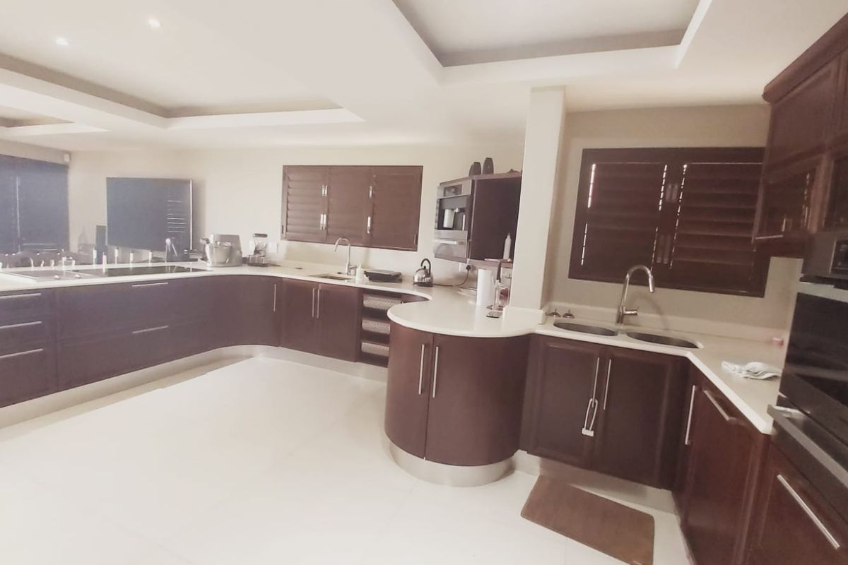 Spacious modern kitchen featuring dark wood cabinetry, stone countertops, double sink, built-in oven, and recessed tray ceiling lighting.
