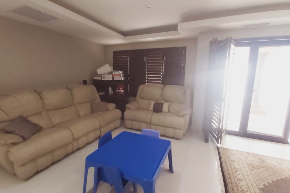 A living room featuring recessed ceiling details, dark plantation shutters, and large glass doors providing access to the exterior.