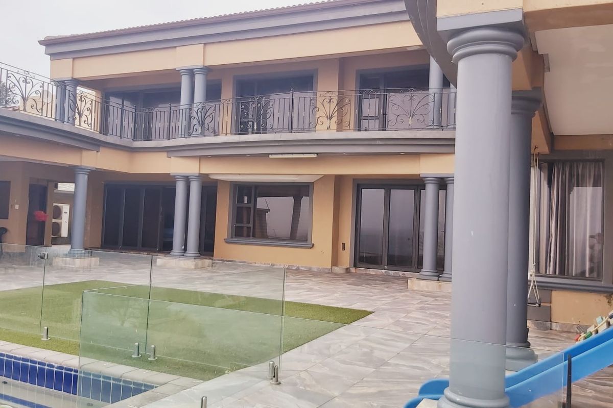 Rear exterior view featuring a covered patio, swimming pool with glass balustrades, and a second-story balcony with wrought iron railings.