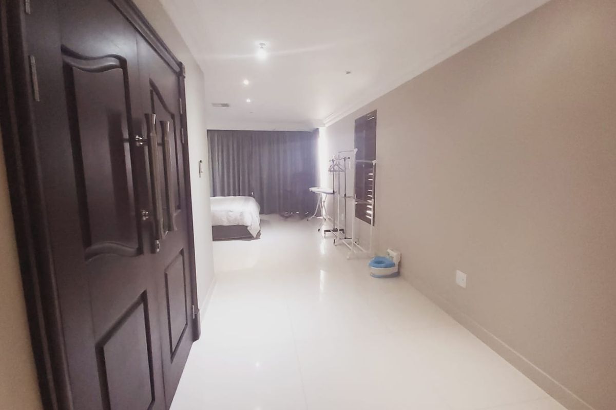 A spacious bedroom featuring tiled flooring, recessed downlighting, and a double door entrance, offering a neutral canvas for interior design.