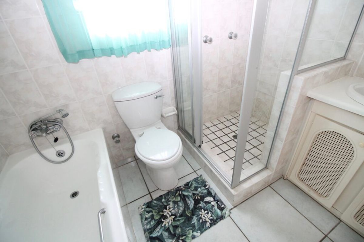 A functional bathroom featuring a built-in bathtub, a separate glass-enclosed shower, a toilet, and a vanity unit with integrated basin.