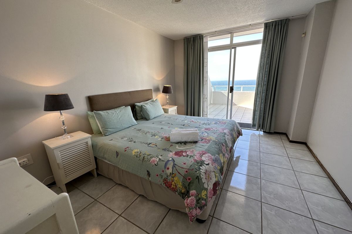 A bright bedroom featuring tiled flooring, a ceiling fan, and sliding glass doors that open onto a private balcony with ocean views.