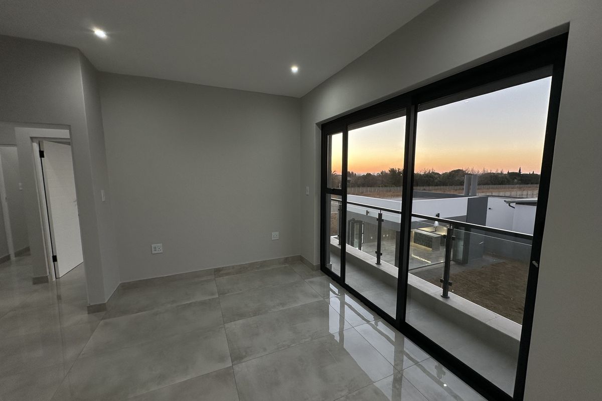 A bright, modern living area featuring large format floor tiles, recessed downlighting, and expansive sliding glass doors opening onto a balcony with sunset views.