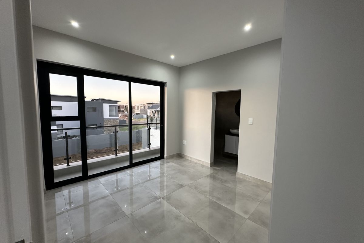 A modern, empty bedroom featuring large sliding glass doors leading to a balcony, recessed ceiling lighting, and polished porcelain floor tiles.