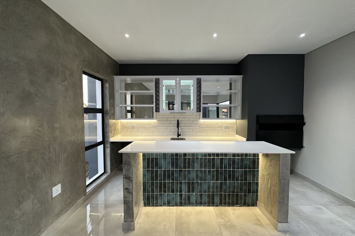 Modern kitchen area featuring a tiled island with stone countertop, integrated sink, under-cabinet lighting, and sleek cabinetry with glass-fronted display sections.