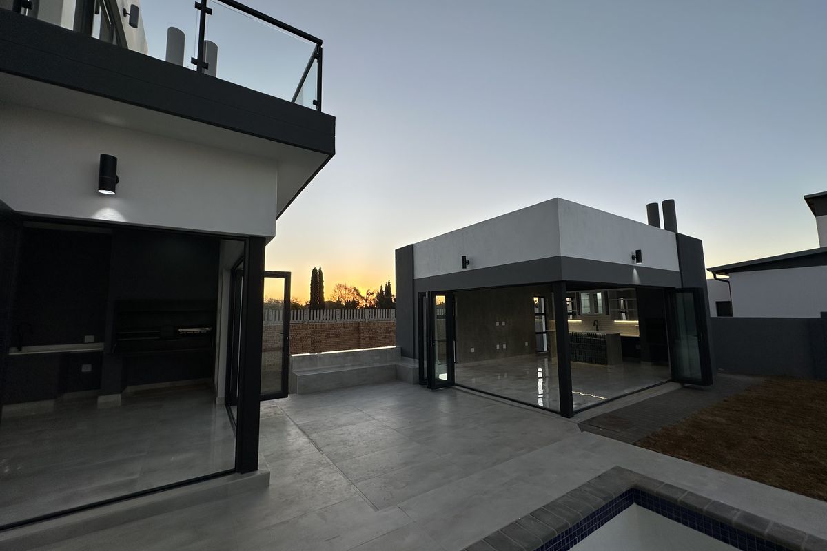 Modern outdoor entertainment area featuring a paved patio, built-in braai, and seamless indoor-outdoor flow through large folding glass doors.