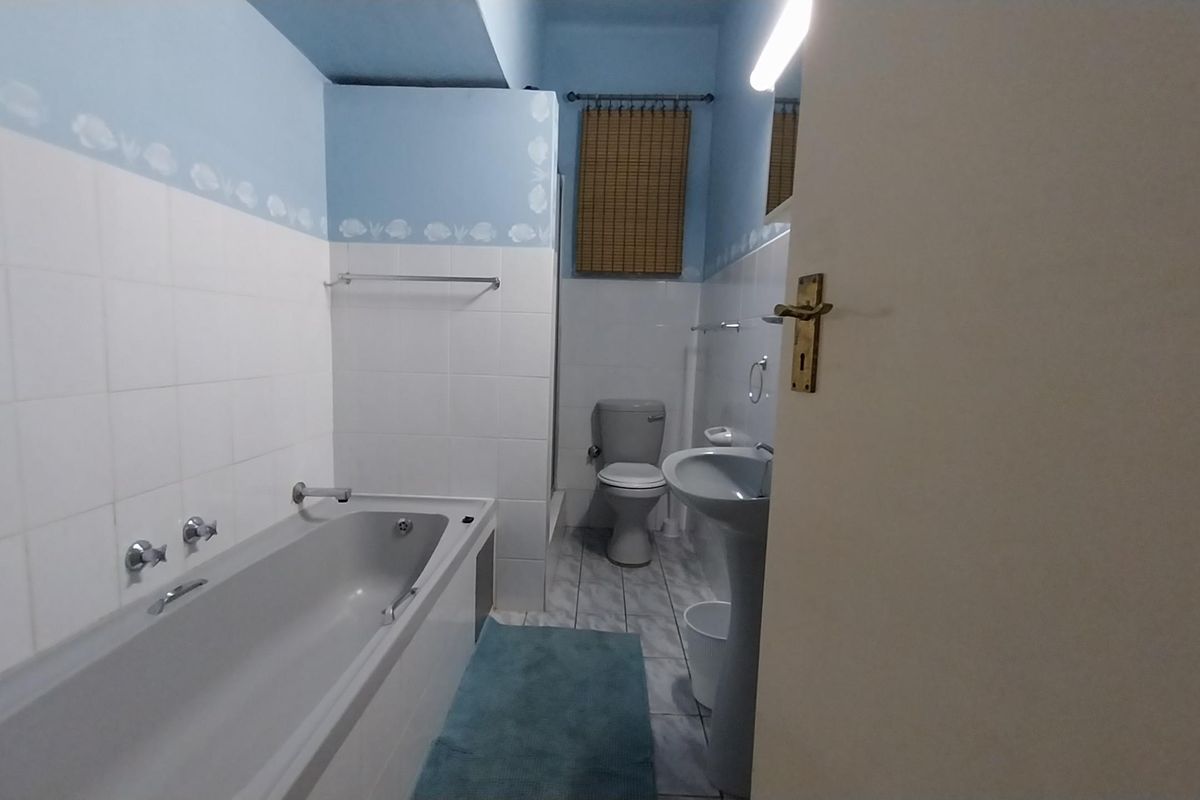 A functional bathroom featuring a standard bathtub, pedestal sink, and toilet with tiled walls and neutral flooring.