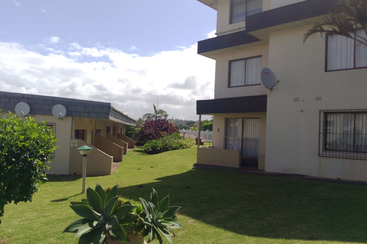 Exterior view of an apartment complex featuring a shared garden area, paved walkways, and multi-story residential units with balcony access.