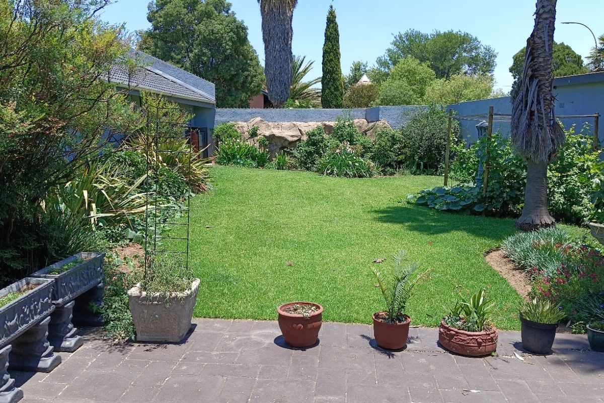 A well-maintained rear garden featuring a paved patio area, lush green lawn, established landscaping, and a decorative rock feature along the boundary wall.