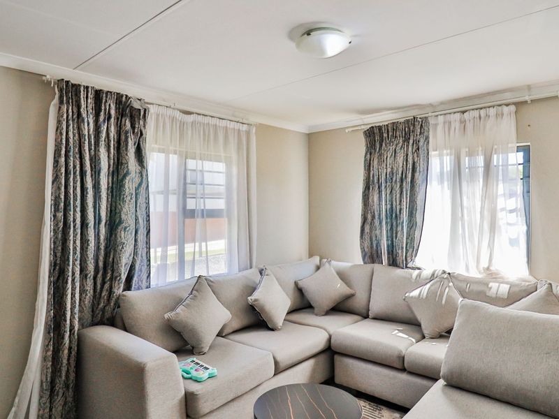 A bright living room featuring neutral walls, dual windows with curtain tracks, and a central ceiling light fixture.