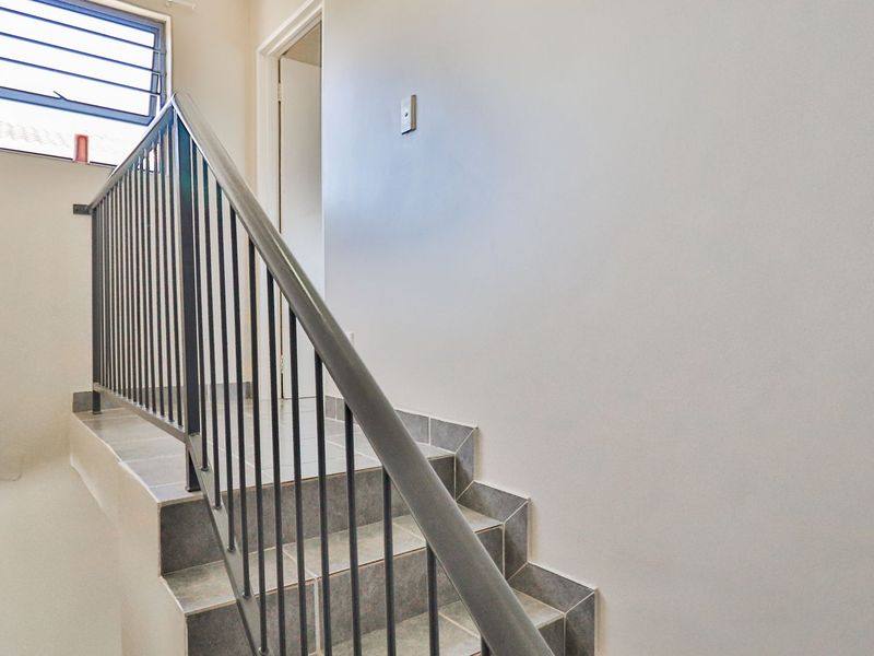 A bright hallway featuring a tiled staircase with a metal balustrade and a louver window providing natural light.