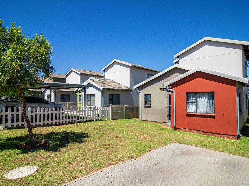 Front view of a townhouse complex featuring a paved driveway, private lawn area, white picket fencing, and a covered carport.