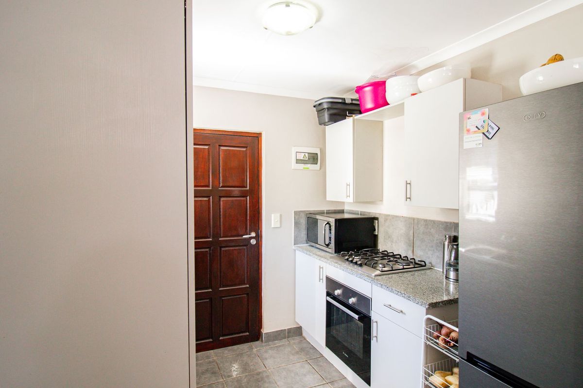 Compact kitchen featuring built-in cabinetry, granite countertops, a gas hob, and a built-in oven, with tiled flooring and direct access via a timber door.