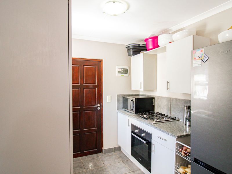 Compact kitchen featuring built-in cabinetry, granite countertops, a gas hob, and a built-in oven, with tiled flooring and direct access via a timber door.