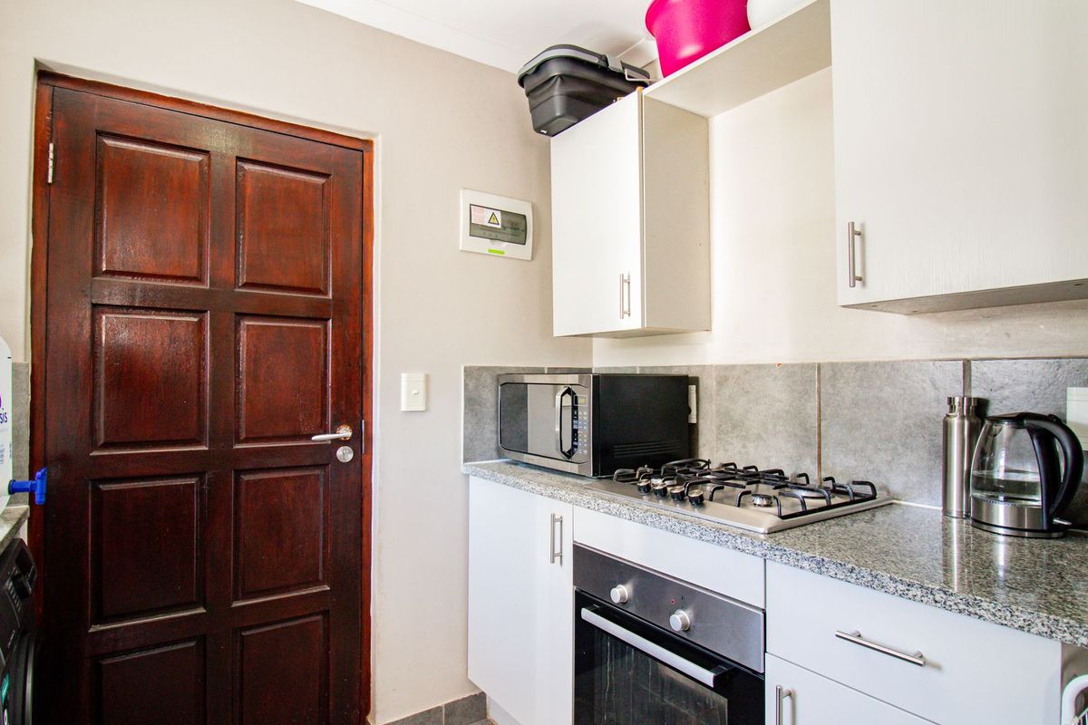 Compact kitchen featuring granite countertops, built-in oven, gas hob, and ample cabinetry, providing a functional workspace with direct access to an exterior door.