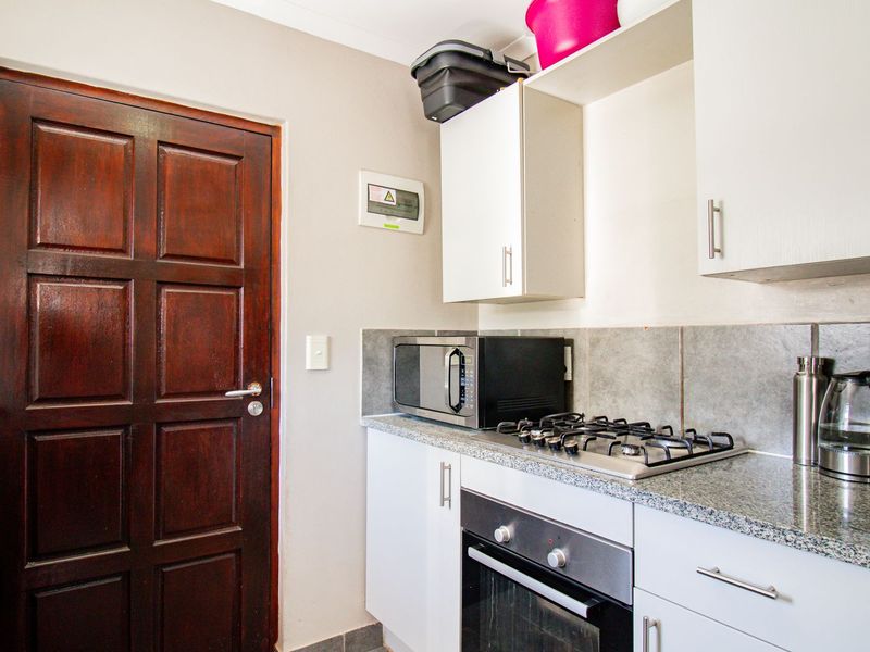 Compact kitchen featuring granite countertops, built-in oven, gas hob, and ample cabinetry, providing a functional workspace with direct access to an exterior door.