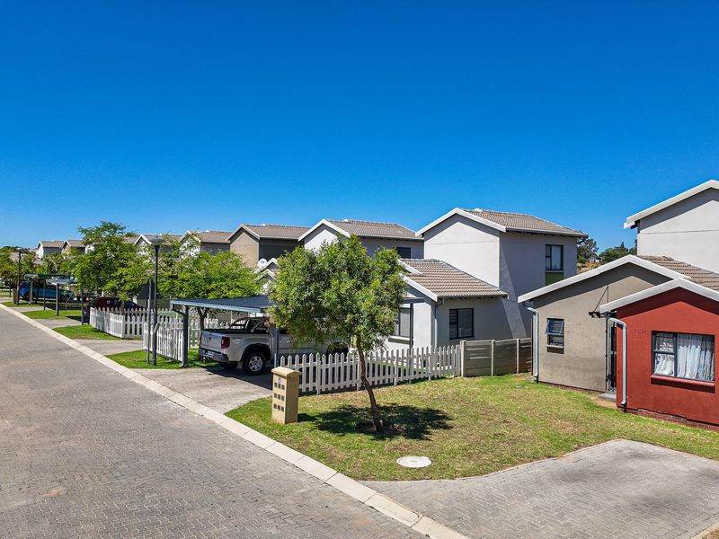 A street-level view of a residential townhouse complex featuring paved driveways, carports, and well-maintained front gardens with picket fencing.