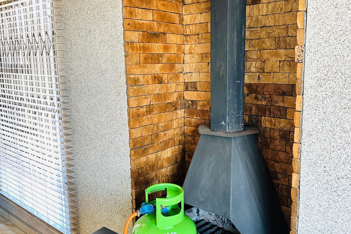 A living area featuring a built-in fireplace with stone cladding, metal flue, and tiled flooring, complemented by fitted venetian blinds.
